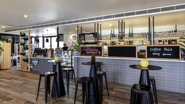 A modern cafe with a bakery display, a coffee bar, and several black stools. - Mercure Bendigo Schaller (Bendigo)