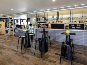 A modern cafe with a bakery display, a coffee bar, and several black stools. - Mercure Bendigo Schaller (Bendigo)