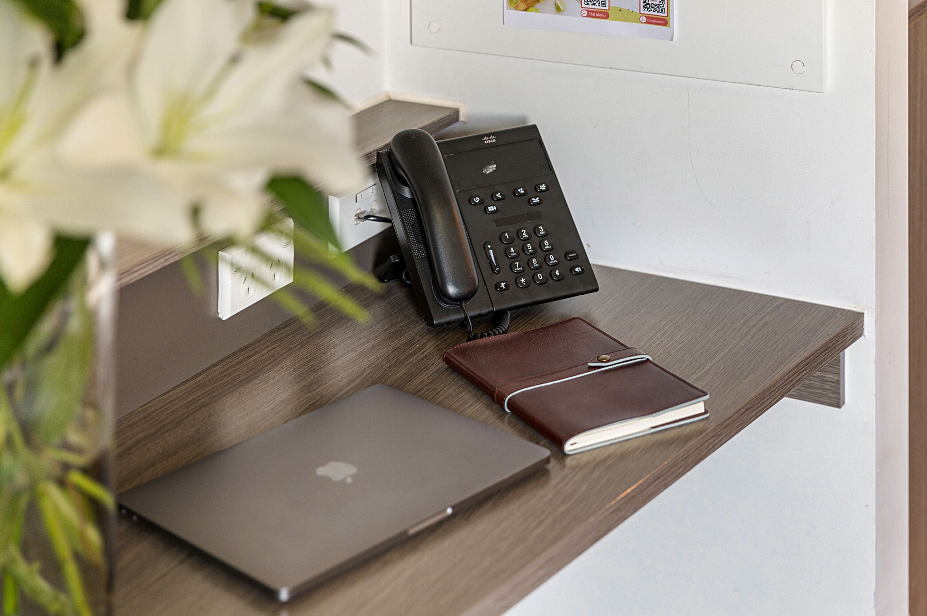 Un escritorio con una computadora portátil, un teléfono y una libreta.