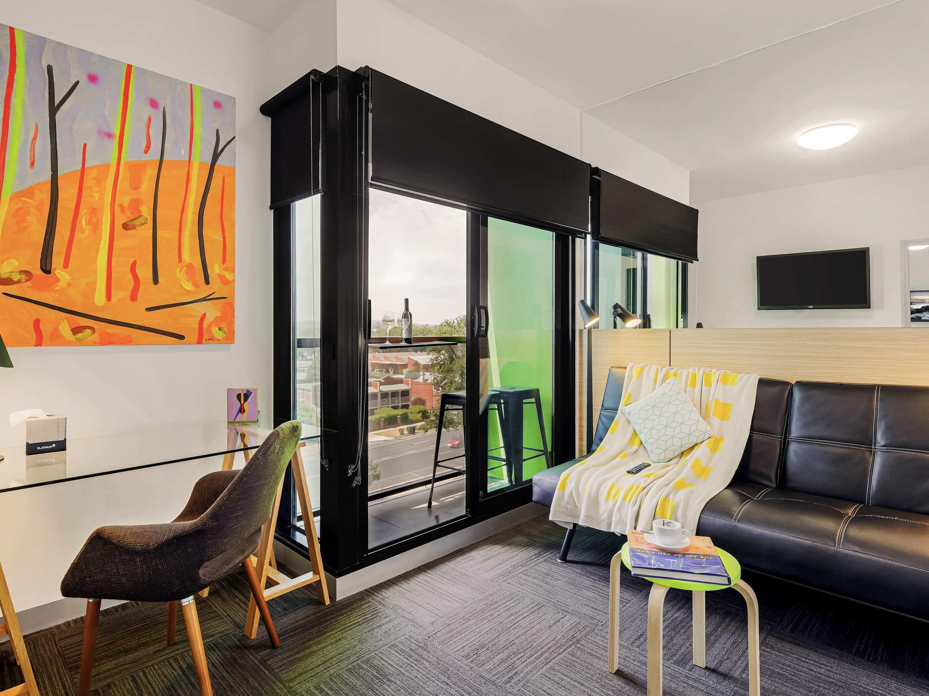 Una habitación moderna con puerta de vidrio que da a un balcón, un sofá de cuero, una mesa de vidrio y una silla.