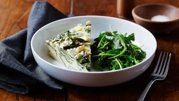 A plate of food with greens and cheese on a wooden table.