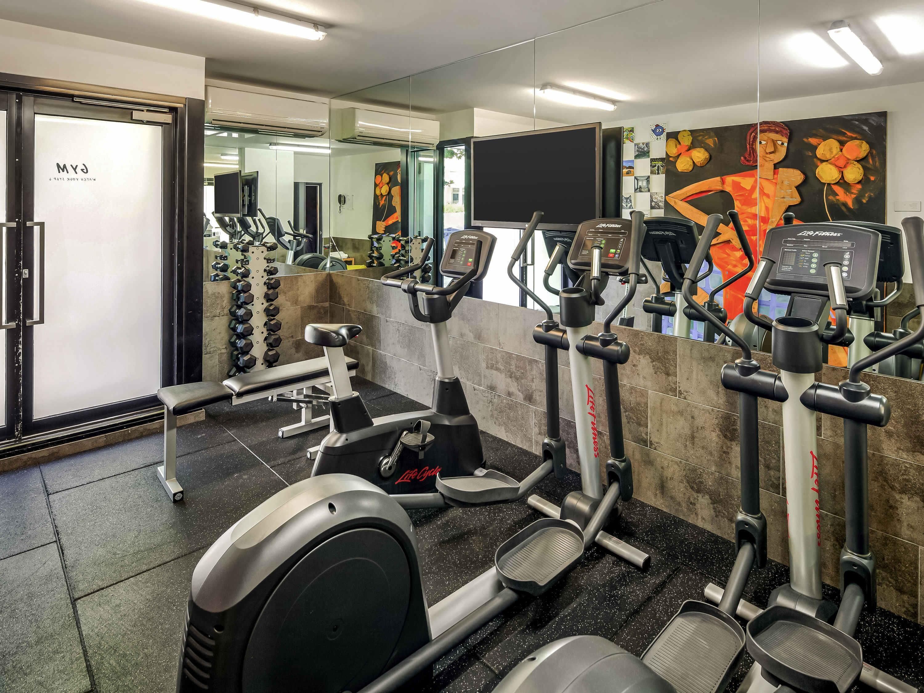 A gym with various exercise equipment, including treadmills and weight machines, and a mirror wall reflecting the space.