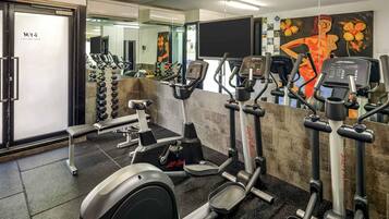 A gym with various exercise equipment, including treadmills and weight machines, and a mirror wall reflecting the space.