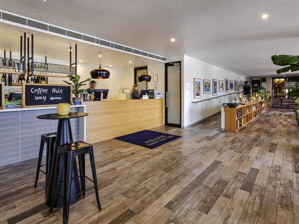 Un hall d’hôtel moderne comprenant un comptoir d’accueil, un bar à café et une galerie d’œuvres d’art.