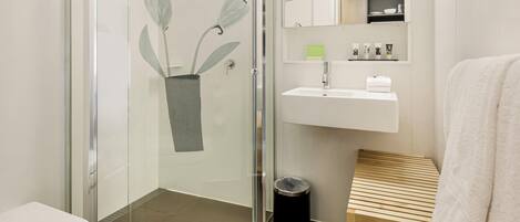 A modern bathroom with a glass shower enclosure, a white sink, and a wooden bench.