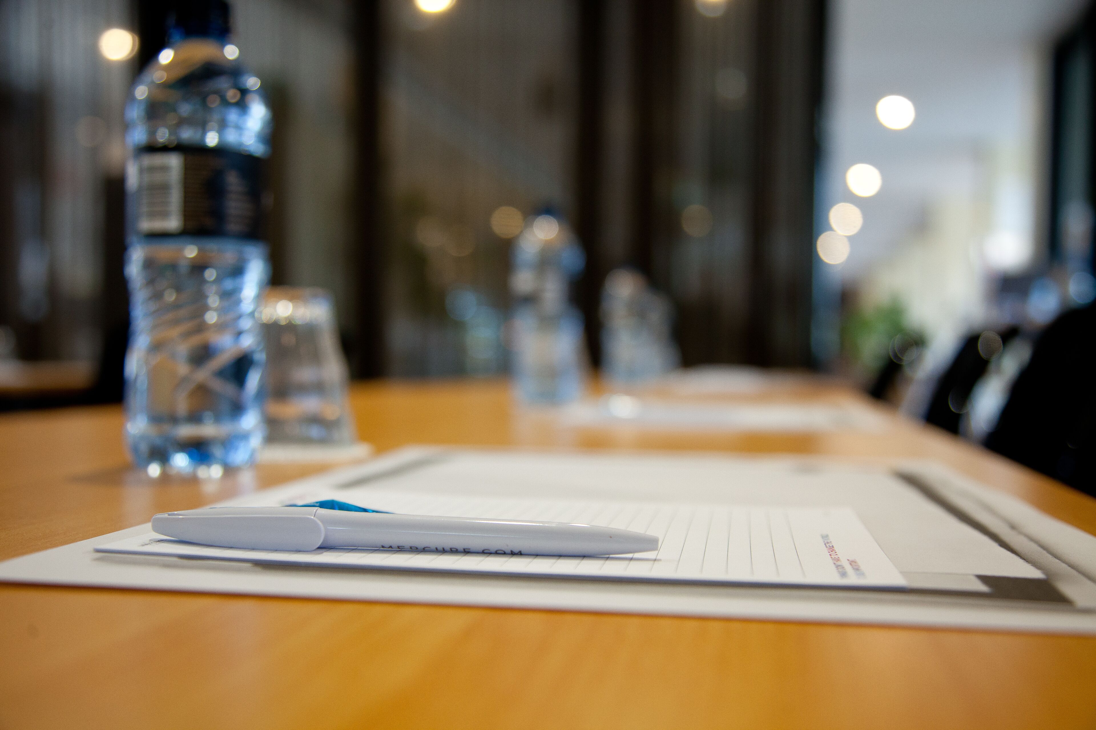 A conference table with a white pen, lined paper, and water bottles.
