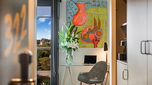 A modern kitchen with a glass door leading to a scenic view, a laptop on a desk, and a vase with flowers on a stand. - Mercure Bendigo Schaller (Bendigo)