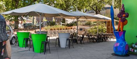 Een terras met meerdere tafels en stoelen, parasols en grote plantenbakken.