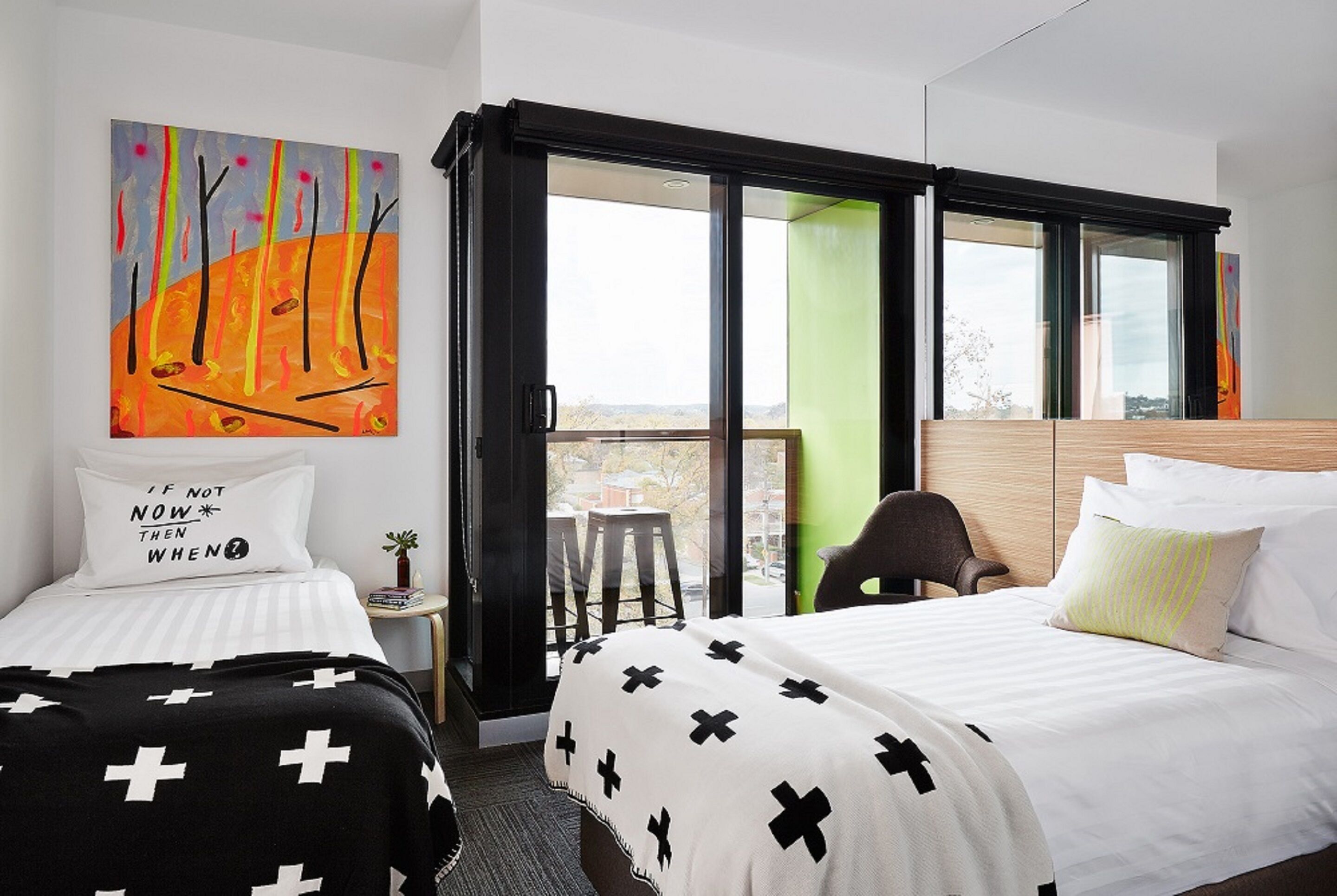 Ein Hotelzimmer mit zwei Betten, einem großen Fenster, einem Bild an der Wand und einem kleinen Tisch mit einer Pflanze.