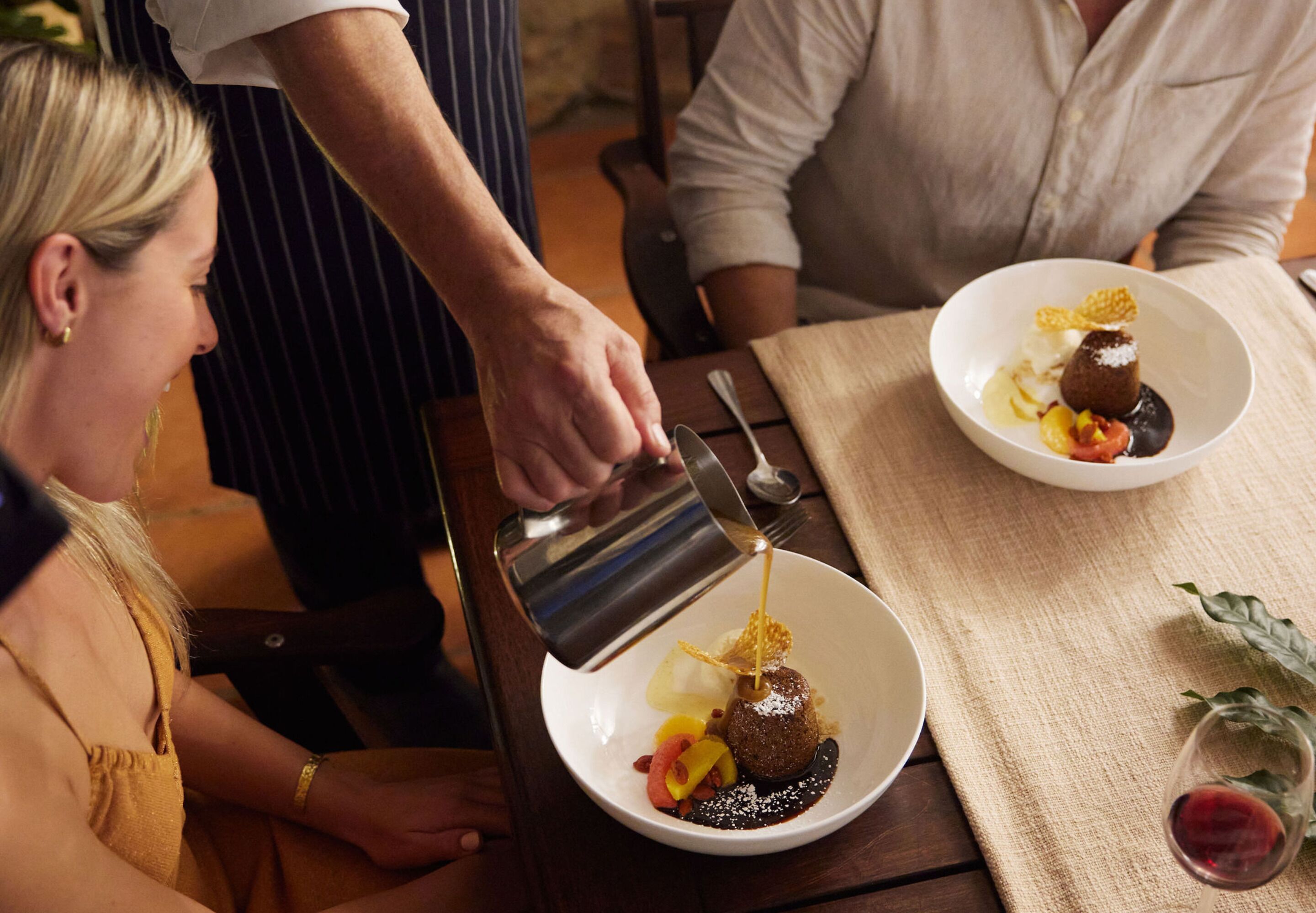 A person pouring a liquid into a dessert on a plate.