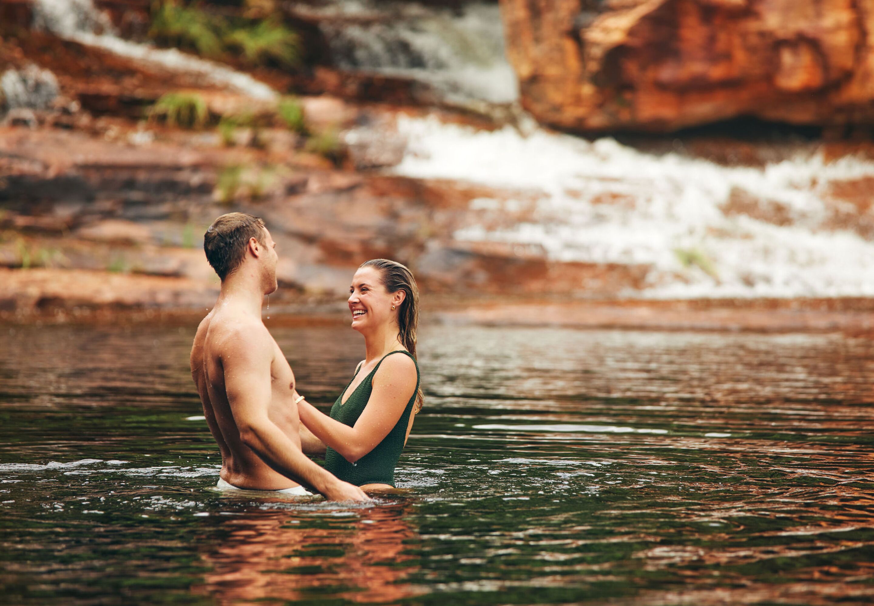Um casal em um rio, cercado por terreno rochoso.