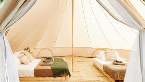 Una carpa con dos camas, cada una con almohadas y mantas, y un tapete tejido en el centro.
