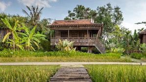 A wooden house with a balcony, surrounded by lush greenery and a rice field. - Sala Lodges (Siem Reap)