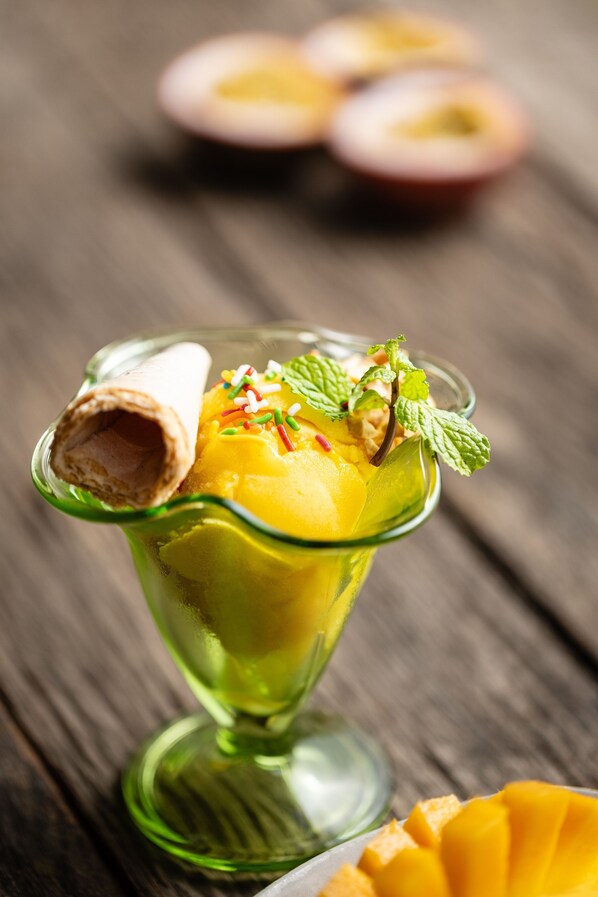 A dessert in a glass bowl with a rolled wafer and mango chunks, garnished with mint and colorful sprinkles. - Sala Lodges (Siem Reap)