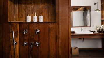 Un mueble de baño de madera con espejo, lavabo y tres botellas de champú, acondicionador y gel de ducha.