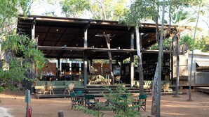 An outdoor seating area with wooden chairs and tables, a covered pavilion, and trees. - Mitchell Falls Wilderness Lodge (Mitchell Plateau)