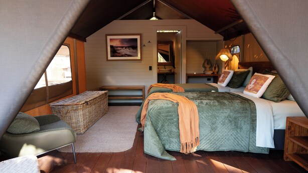 A cozy, triangular tent-style bedroom with a bed, a chair, a small table, and a basket. - Mitchell Falls Wilderness Lodge (Mitchell Plateau)