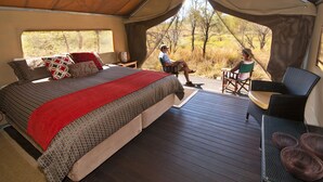 Een tentaccomodatie met een bed, een zithoek en uitzicht op de natuur.