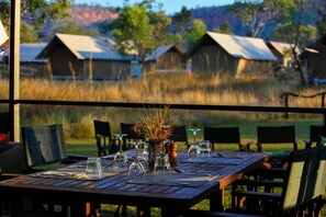 Mesa de comedor al aire libre con sillas, un jarrón con plantas secas y una vista de edificios rústicos al fondo.