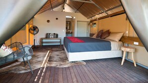 A cozy attic bedroom with a bed, a chair, a small table, and a fan.