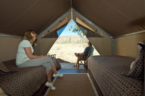 Uma tenda com duas camas, vista para o deserto e uma pessoa sentada numa cadeira.