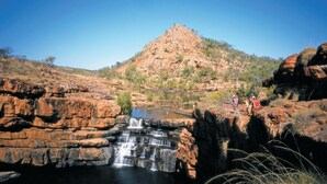 A natural landscape with a waterfall, rocky terrain, and a hill in the background.