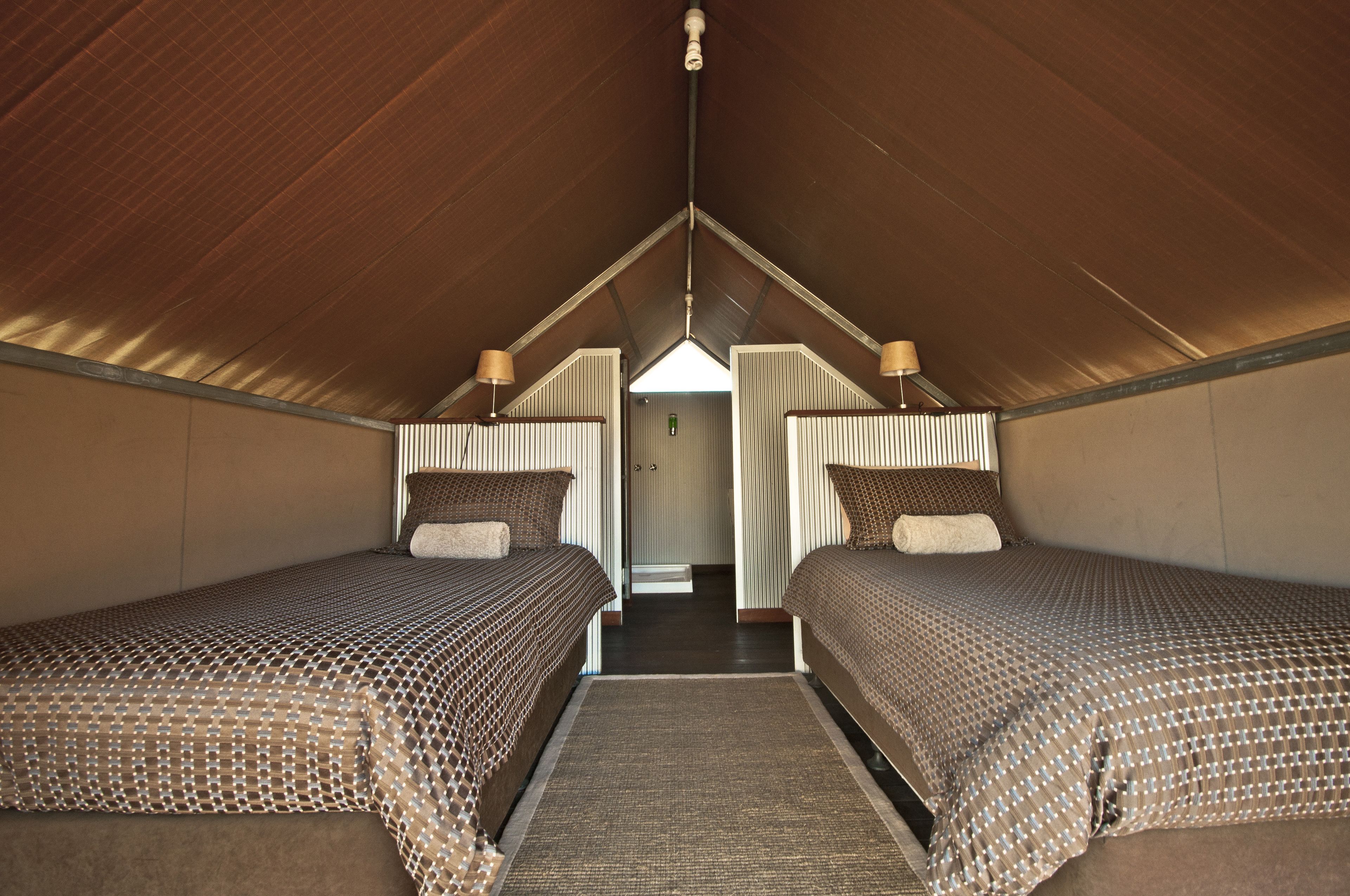 A room with two beds, a wooden ceiling, and a door leading to another area.