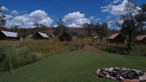 A rural setting with several rustic cabins, a grassy field, and a clear sky.