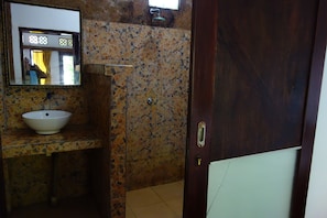 A bathroom with a mosaic tile wall, a white sink, and a door with a brass handle. - Banana Leaf Bungalows (Gili Trawangan)
