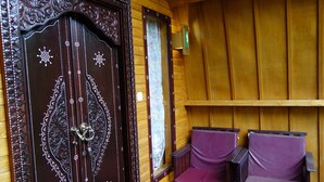 A wooden door with intricate carvings and a small window. There are two purple chairs with wooden armrests and a small table with a vase of flowers. - Banana Leaf Bungalows (Gili Trawangan)
