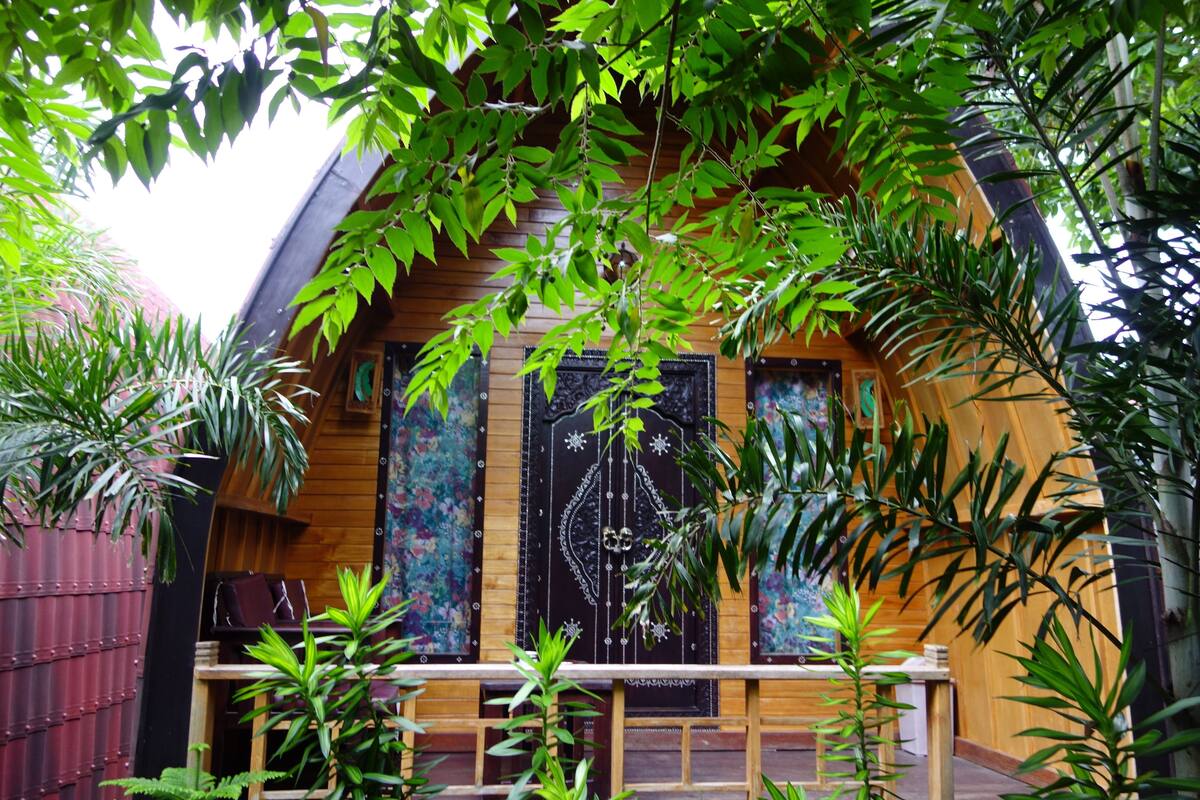 Une cabane en bois dotée d’un balcon, entourée d’une végétation luxuriante.