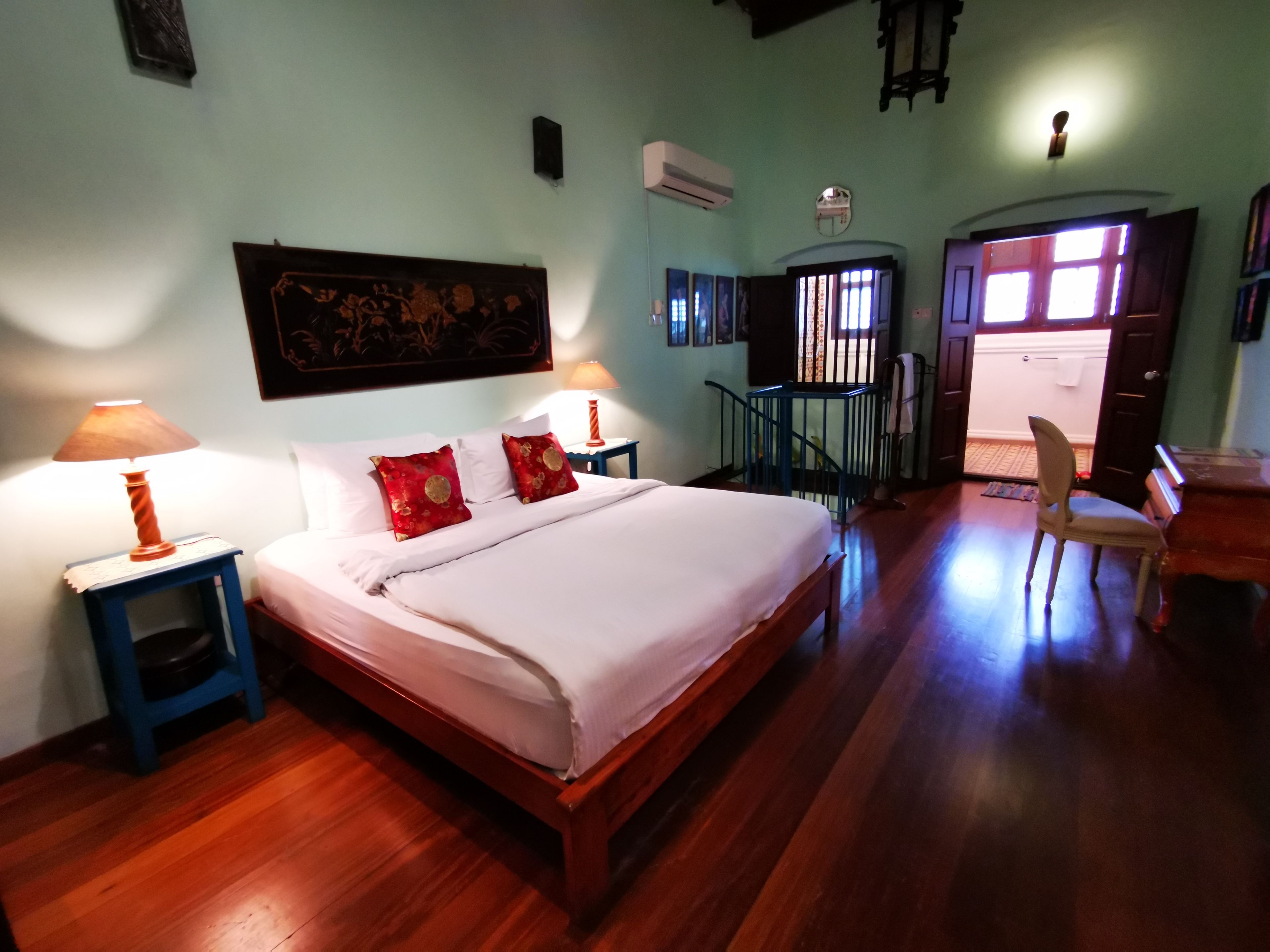 A bedroom with a wooden bed, two bedside tables with lamps, a chair, and a staircase leading to an outdoor area.