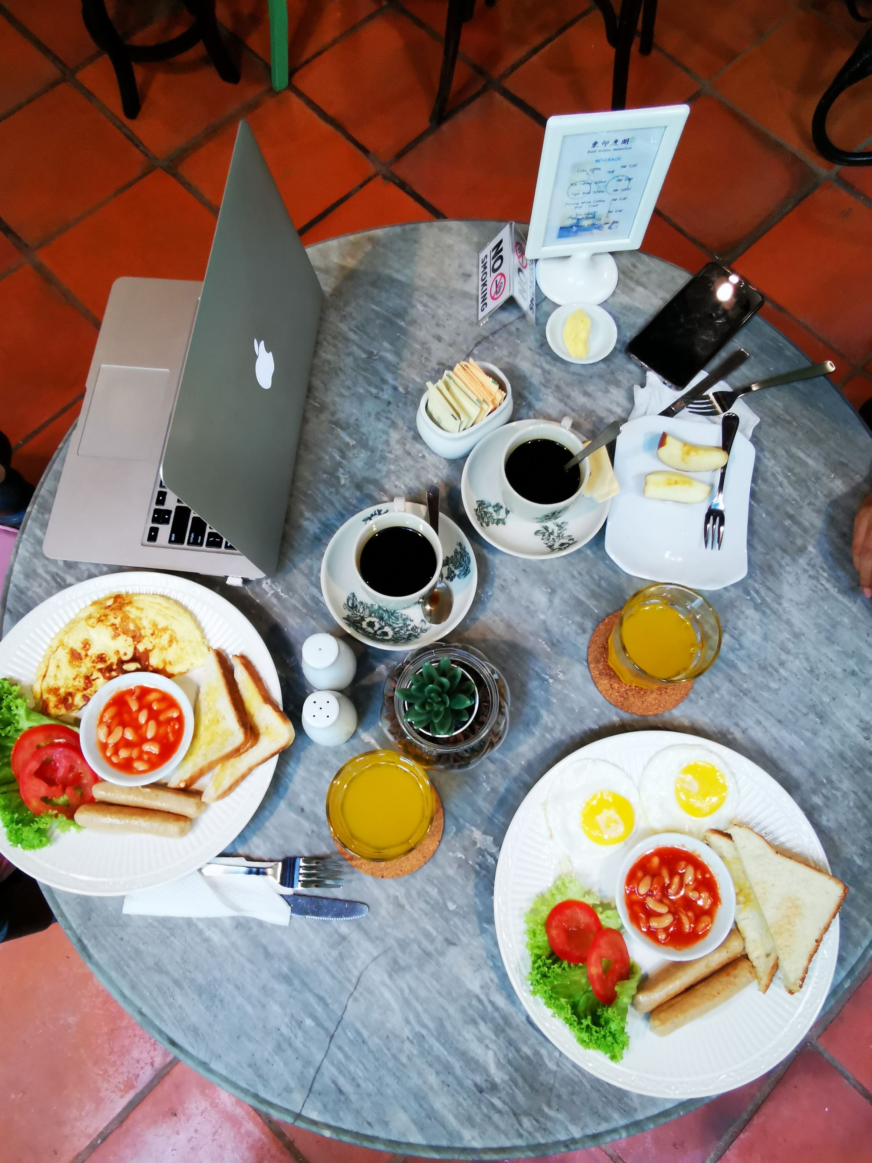 A table with a laptop, various breakfast items, and a mobile phone.