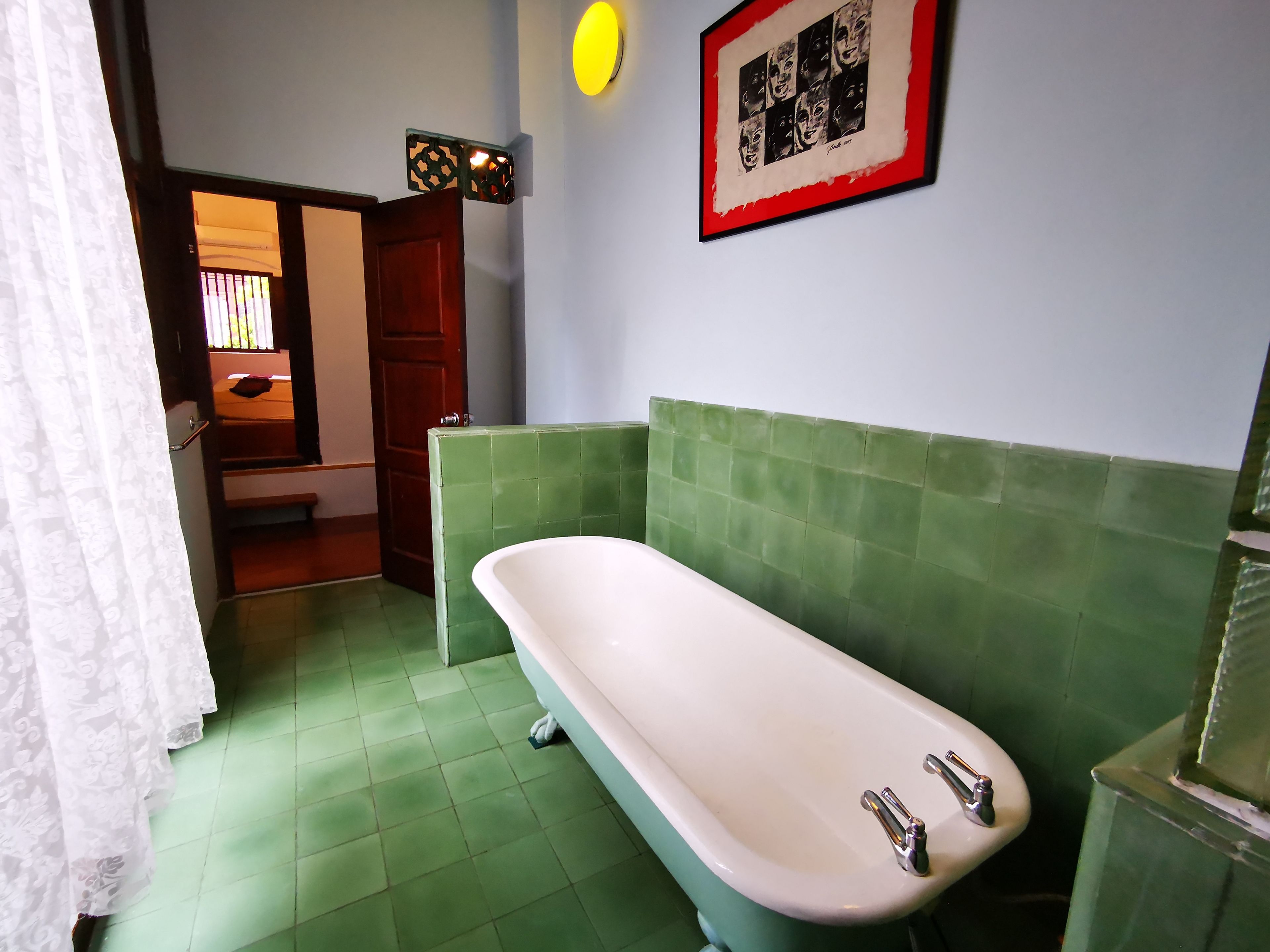 Ein Badezimmer mit grüner Fliesenwand, einer weißen Badewanne und einem gerahmten Bild an der Wand.