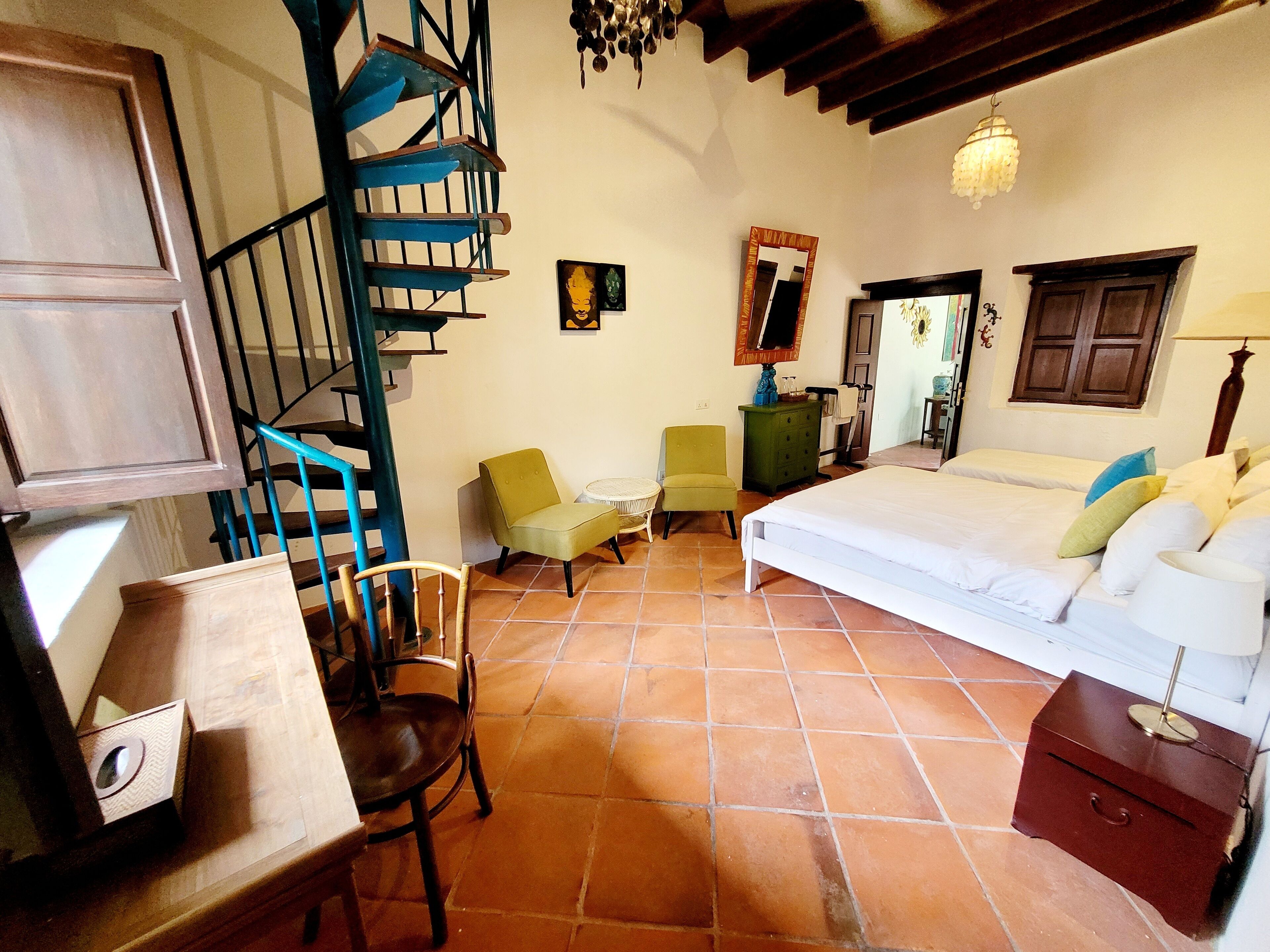 A bedroom with a bed, a chair, a desk, a dresser, a mirror, and a spiral staircase.