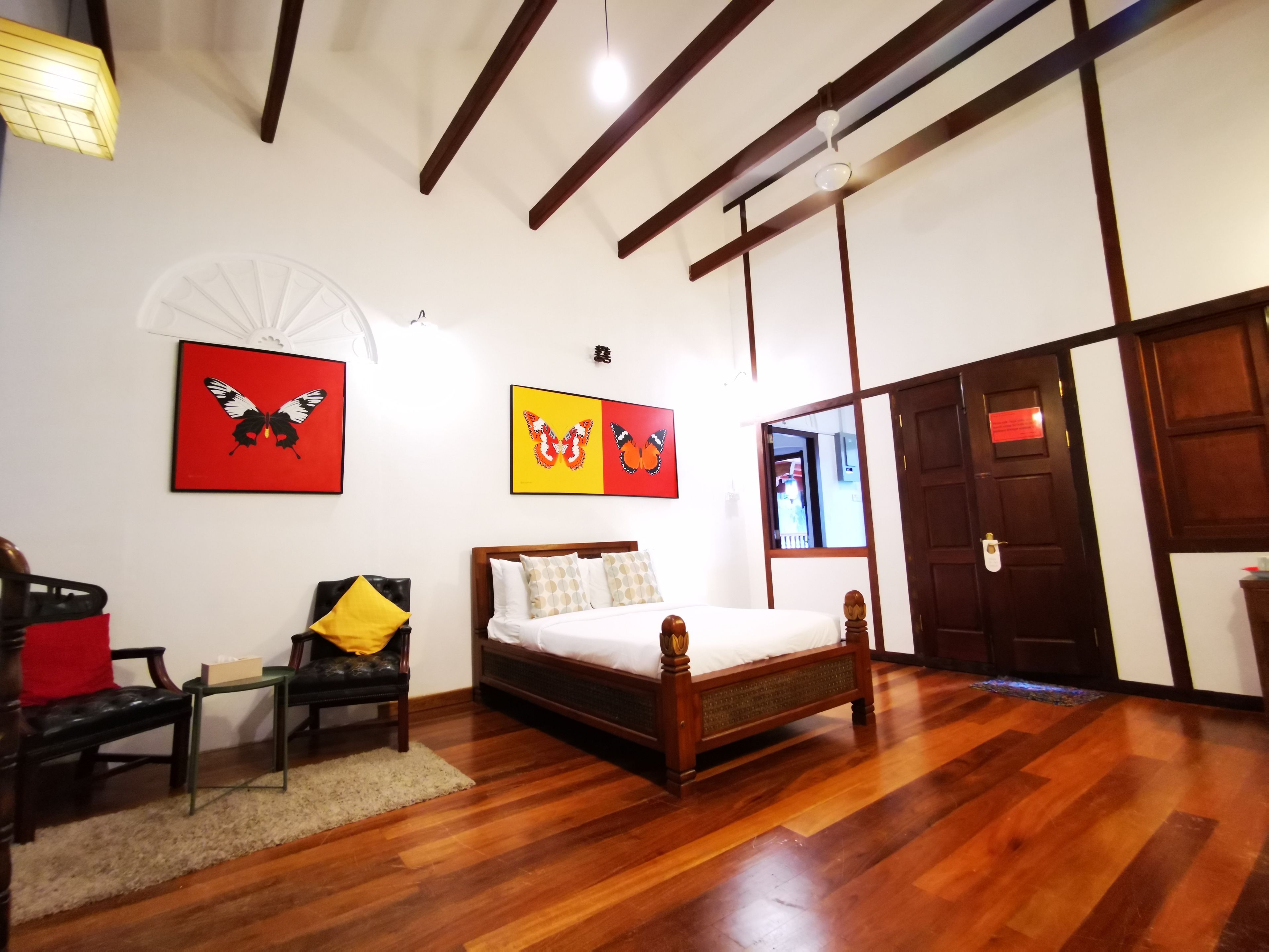 A bedroom with a wooden bed, a chair, a small table, and two butterfly-themed wall art pieces.