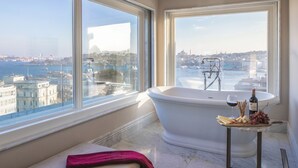 Une salle de bain avec une baignoire, un comptoir en marbre sur lequel se trouvent une bouteille de vin et des raisins, et un banc avec une serviette rose.