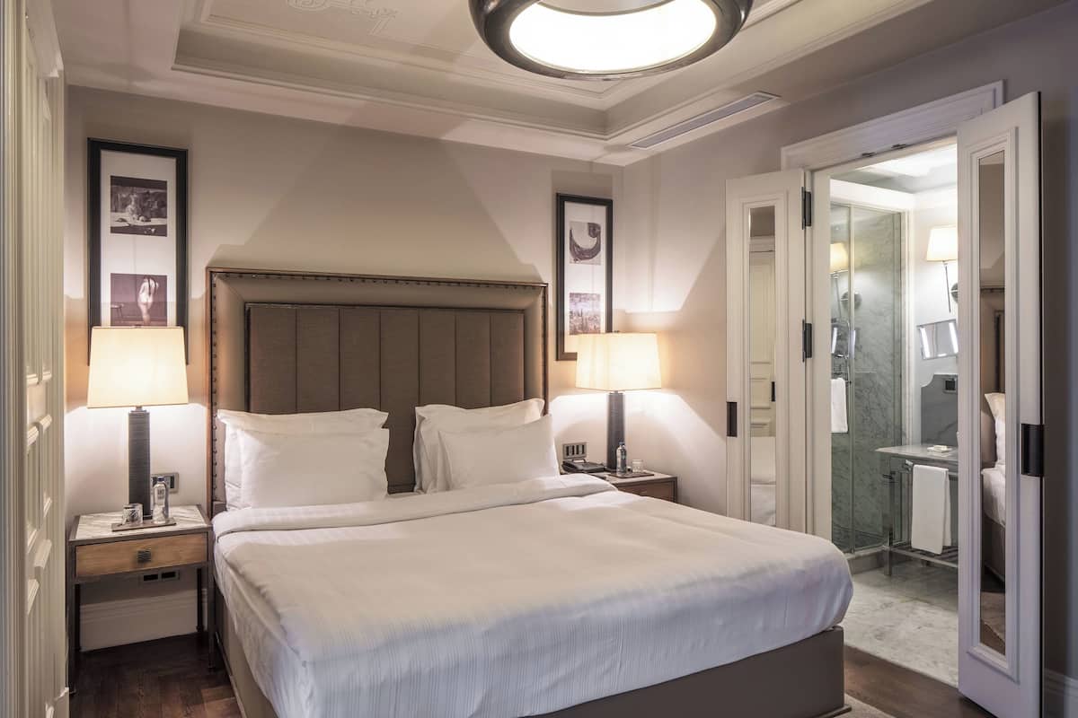 A hotel room with a large bed, two bedside tables, and a nightstand. There is a bathroom visible through an open door.