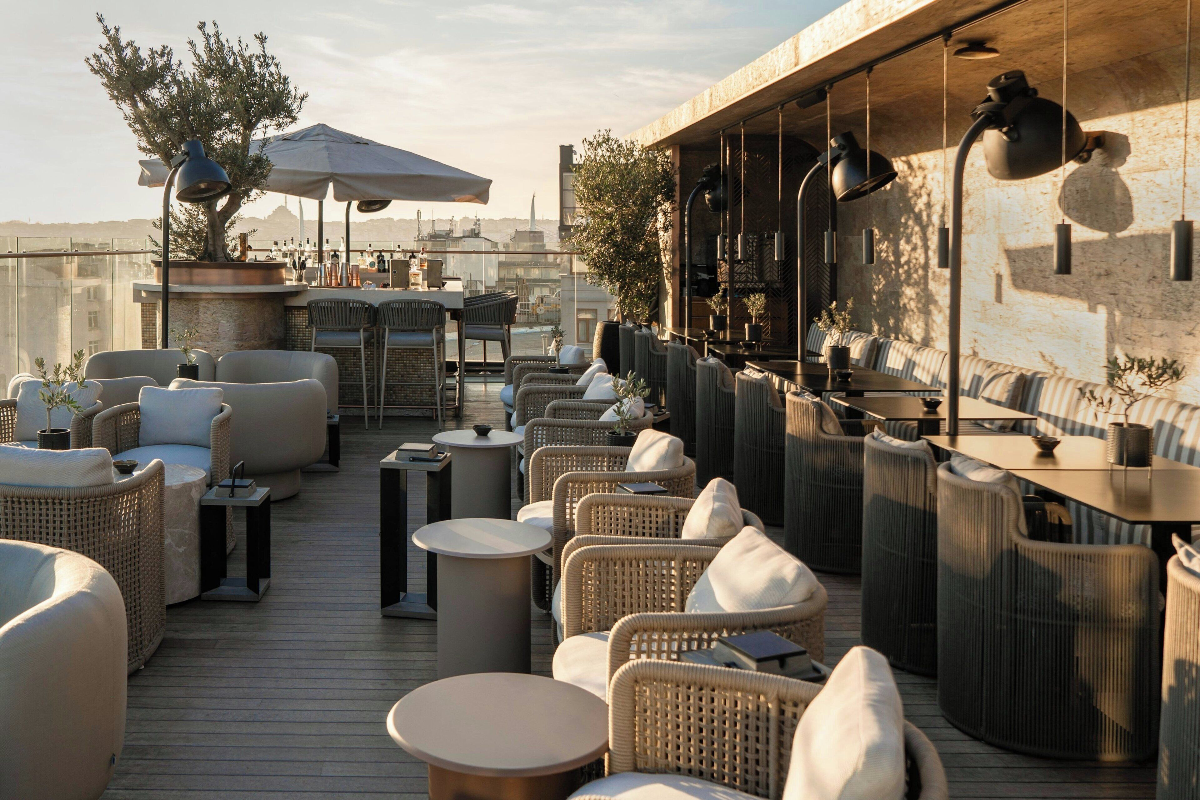 A rooftop terrace with wicker furniture, round tables, and hanging lamps.