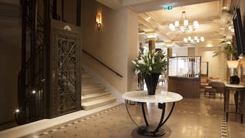Una hall con una scala, un tavolo rotondo con un vaso di fiori e una reception.