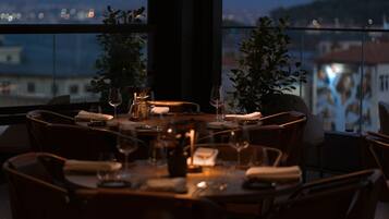 Comedor con una mesa dispuesta para cuatro personas, rodeada de sillas, con vistas a edificios y una colina al fondo.