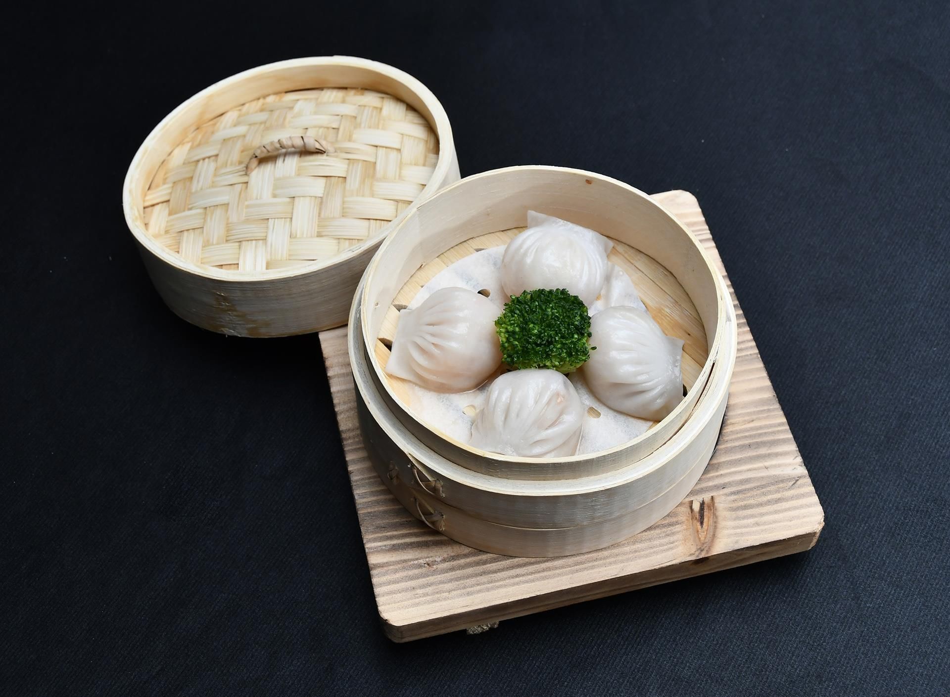 Two bamboo steamer baskets with white dumplings and a green garnish on a wooden board.