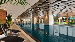 An indoor swimming pool with modern design, including a unique ceiling pattern and large windows offering views of the outdoors.