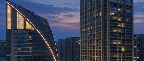 A modern hotel with a curved facade and a tall adjacent building with illuminated windows.