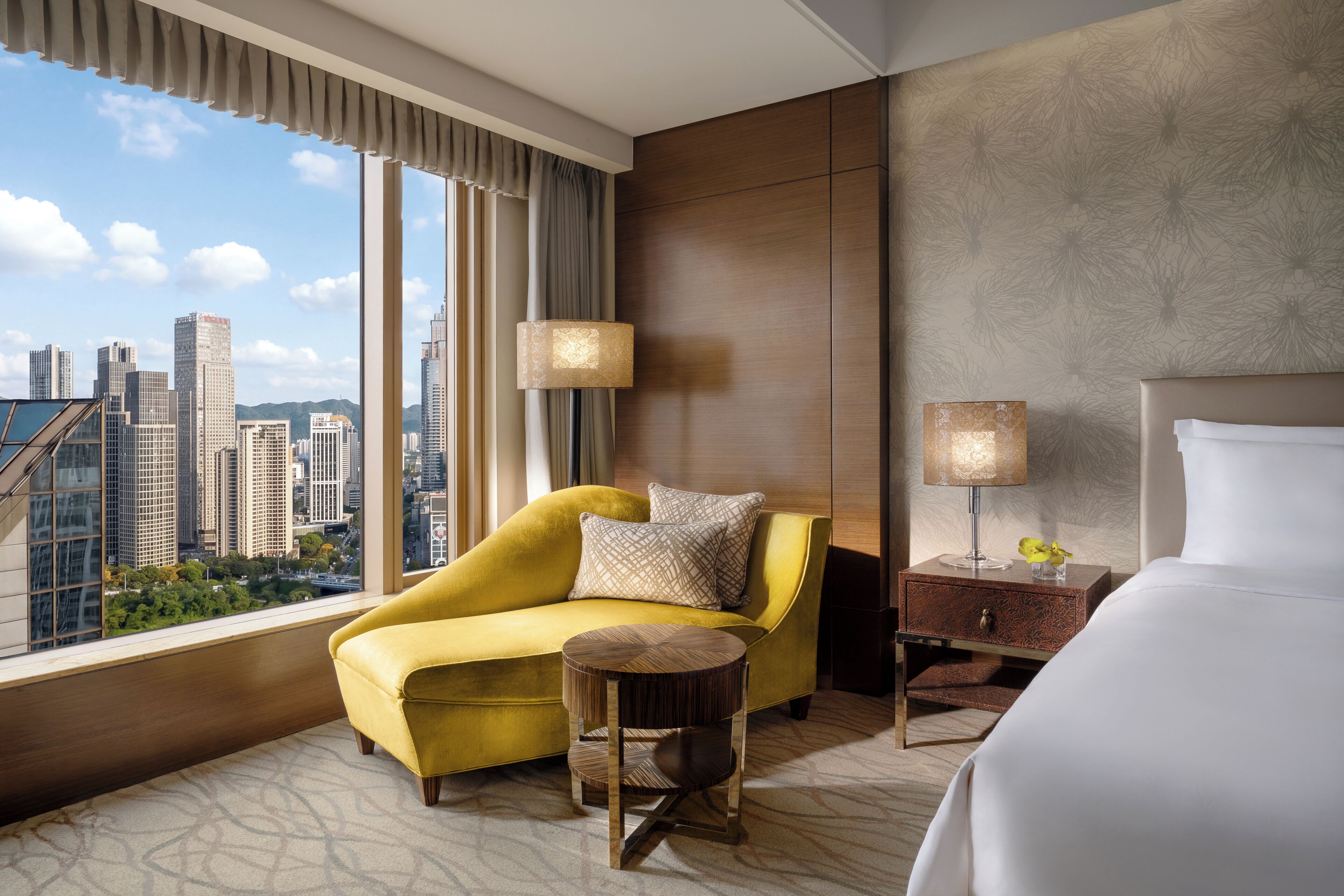 A hotel room with a city view, a sofa, a round table, a lamp, and a bed.