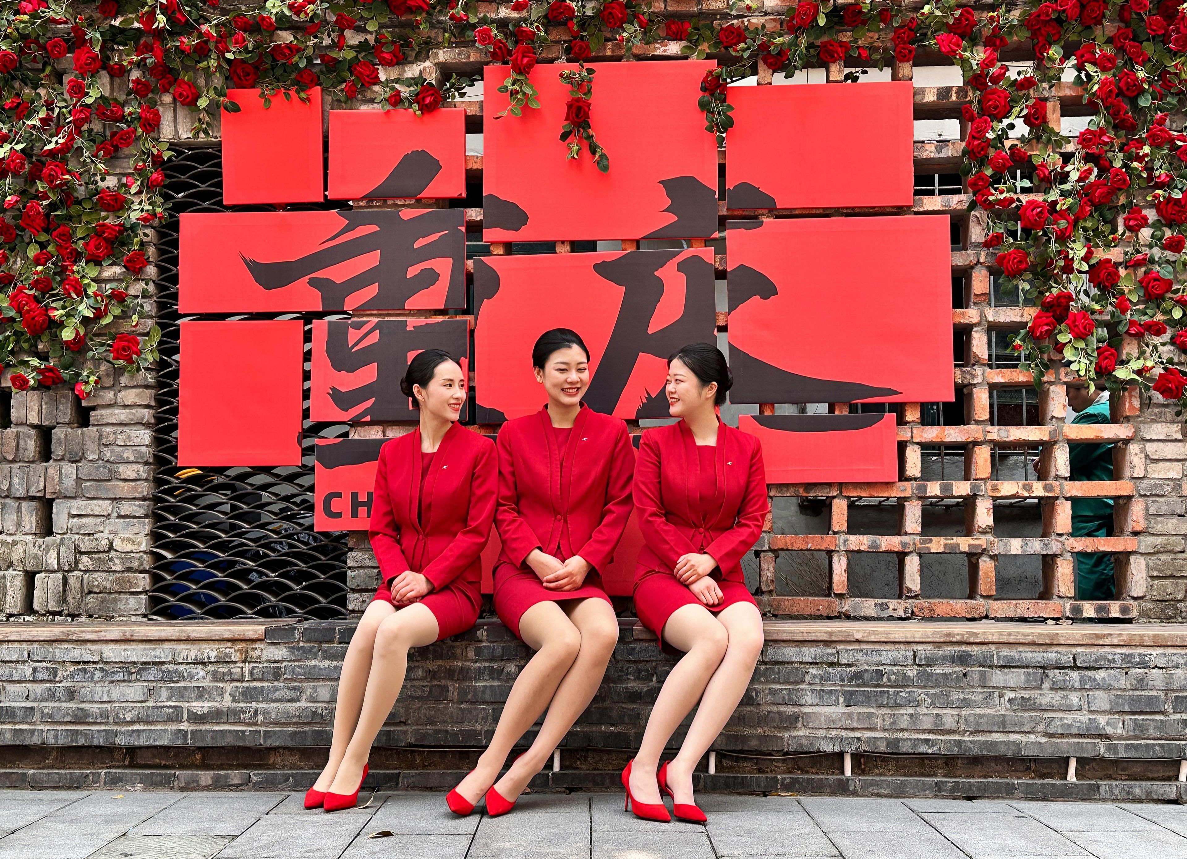 Three individuals seated on a bench with a red backdrop featuring Chinese characters.