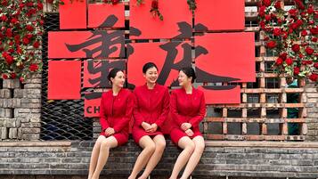 Three individuals seated on a bench with a red backdrop featuring Chinese characters.