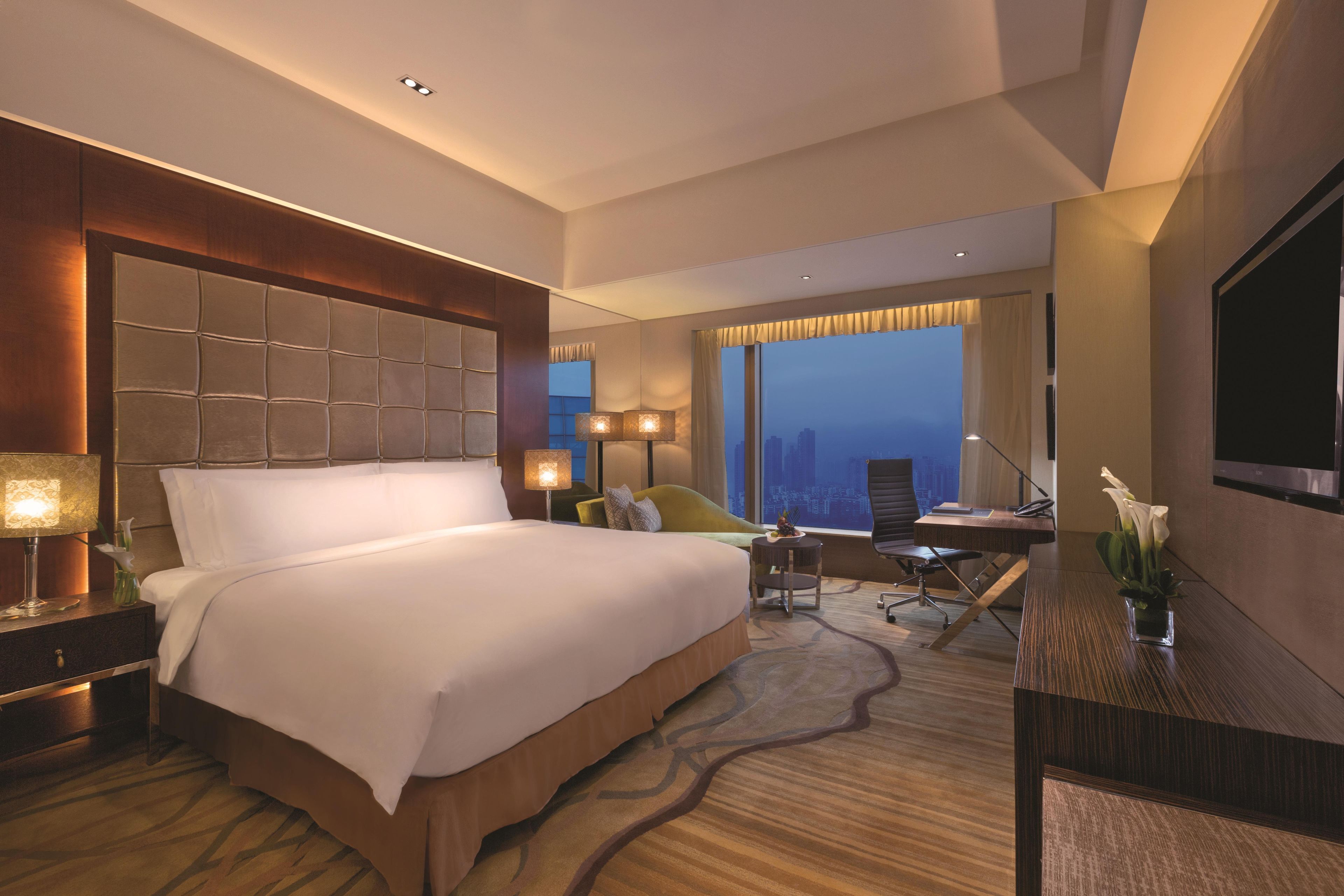 Habitación de hotel con una cama grande, un escritorio con silla, televisión y vistas a la ciudad.