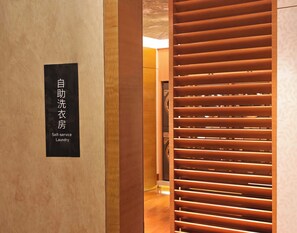 A self-service laundry area with a sign in a foreign language and a wooden slatted partition.