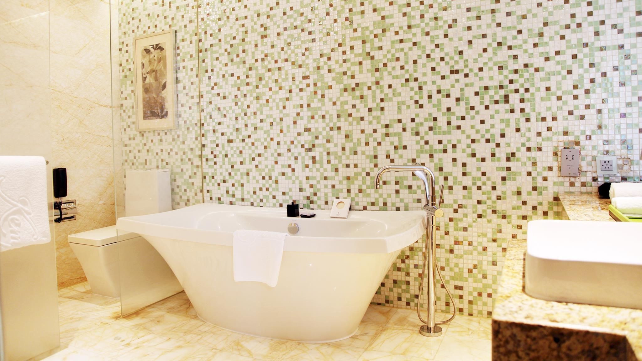 Een moderne badkamer met een vrijstaand bad, een aparte wastafel en een betegelde mozaïekwand.